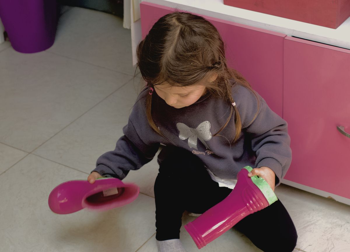 Una niña pequeña se pone sola sus botas pantaneras